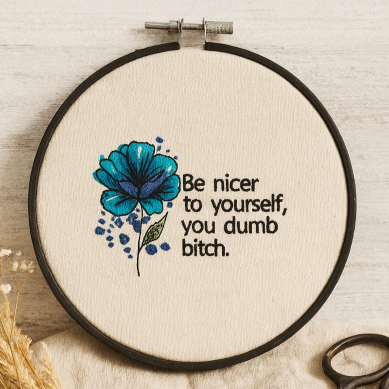 Embroidery hoop with blue floral design and text on a wooden surface with scissors and thimble.