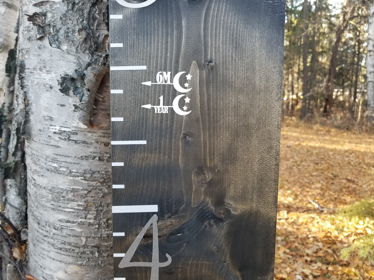 A Little Prairie Craft Co. Stars & the Moon Height Marking Arrows thermometer on a tree in the woods.