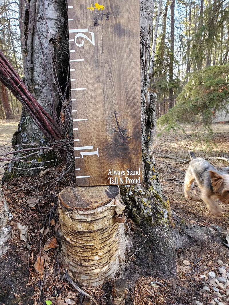 A dog is standing next to a Little Prairie Craft Co. Always Stand Tall & Proud Decal wooden growth chart.