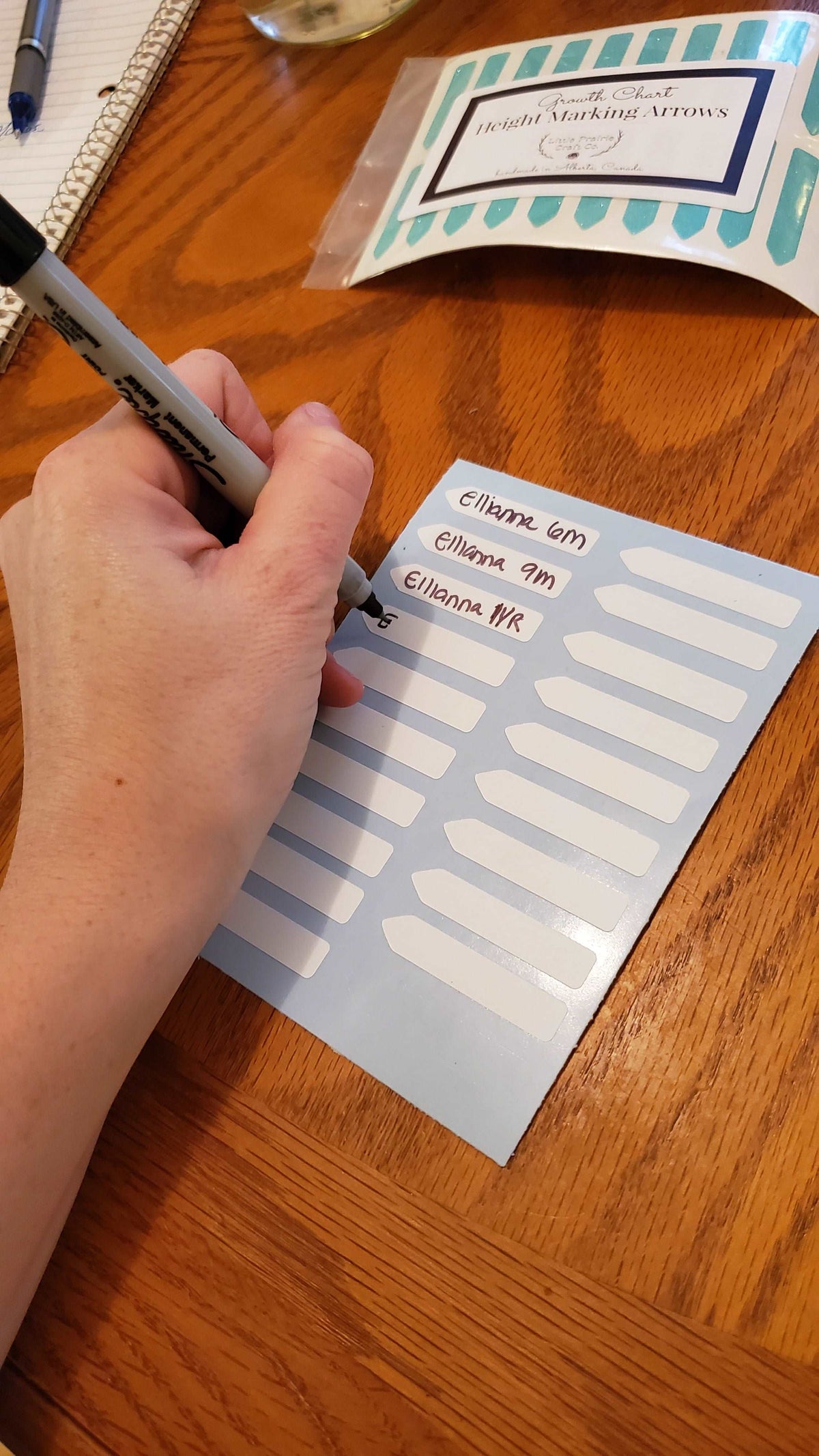 A person writing on a piece of paper with the Little Prairie Craft Co. Blank Write Yourself Height Marking Arrows pen.
