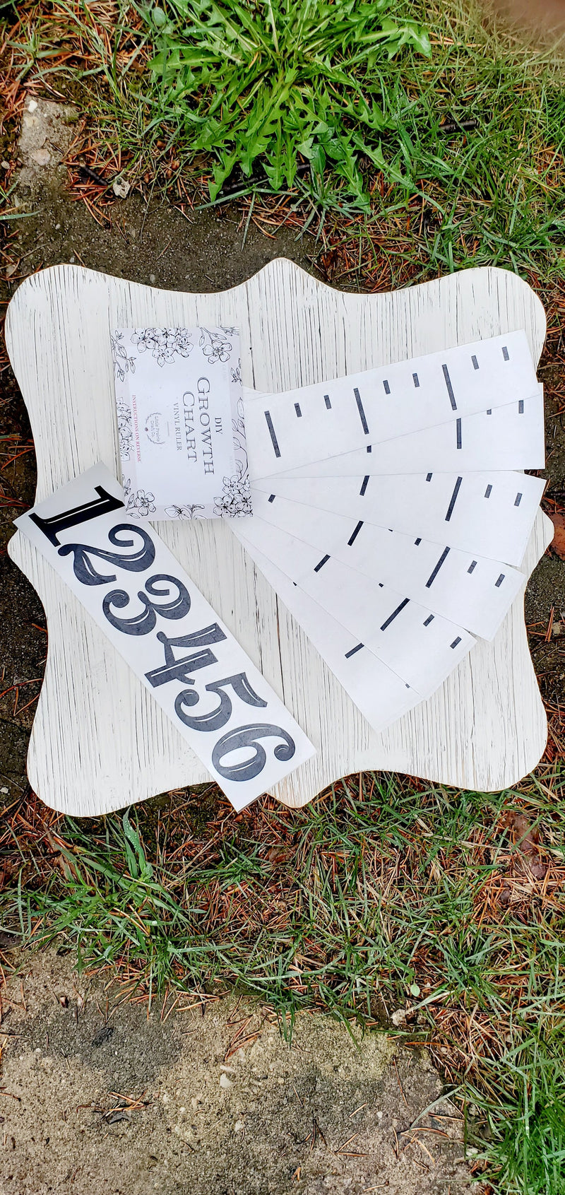 A piece of wood with an Imperial | EASY DIY Growth Chart Vinyl Ruler Kit from Little Prairie Craft Co. on it in the grass.