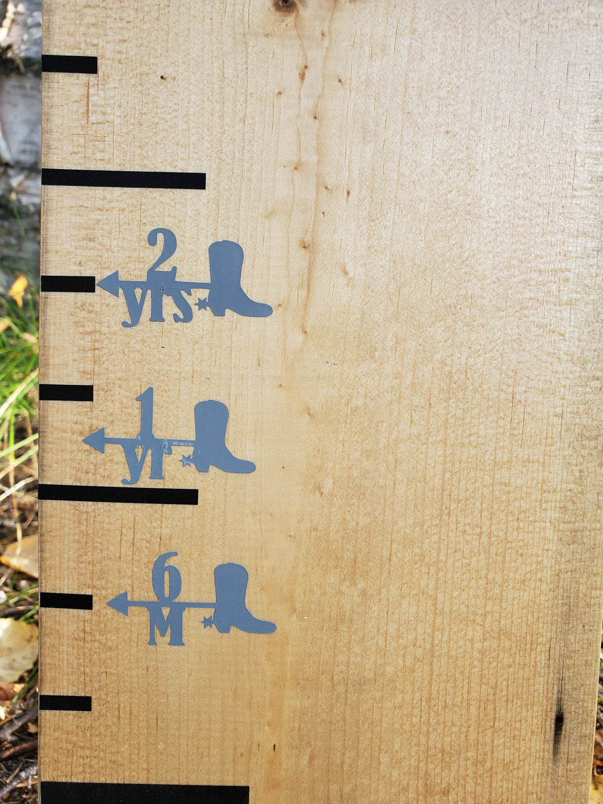 A wooden board with a Cowboy Boot Height Marking Arrows ruler and a pair of Little Prairie Craft Co. cowboy boots.