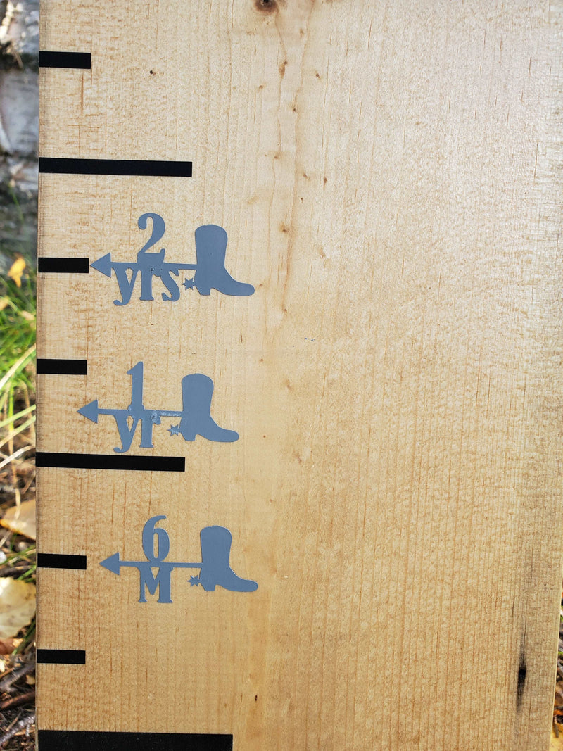 A wooden board with a Cowboy Boot Height Marking Arrows ruler and a pair of Little Prairie Craft Co. cowboy boots.