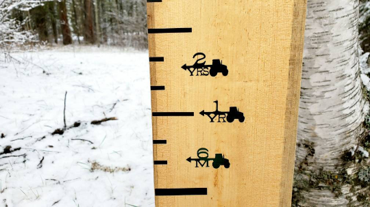 A Tractor Height Marking Arrows ruler by Little Prairie Craft Co. with a snow covered tree in the background.
