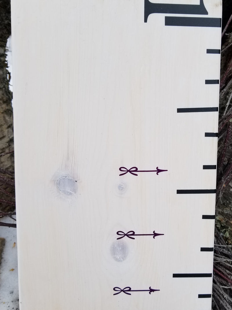 A wooden ruler with Lil Mini Bow Height Marking Arrows from Little Prairie Craft Co. on it.